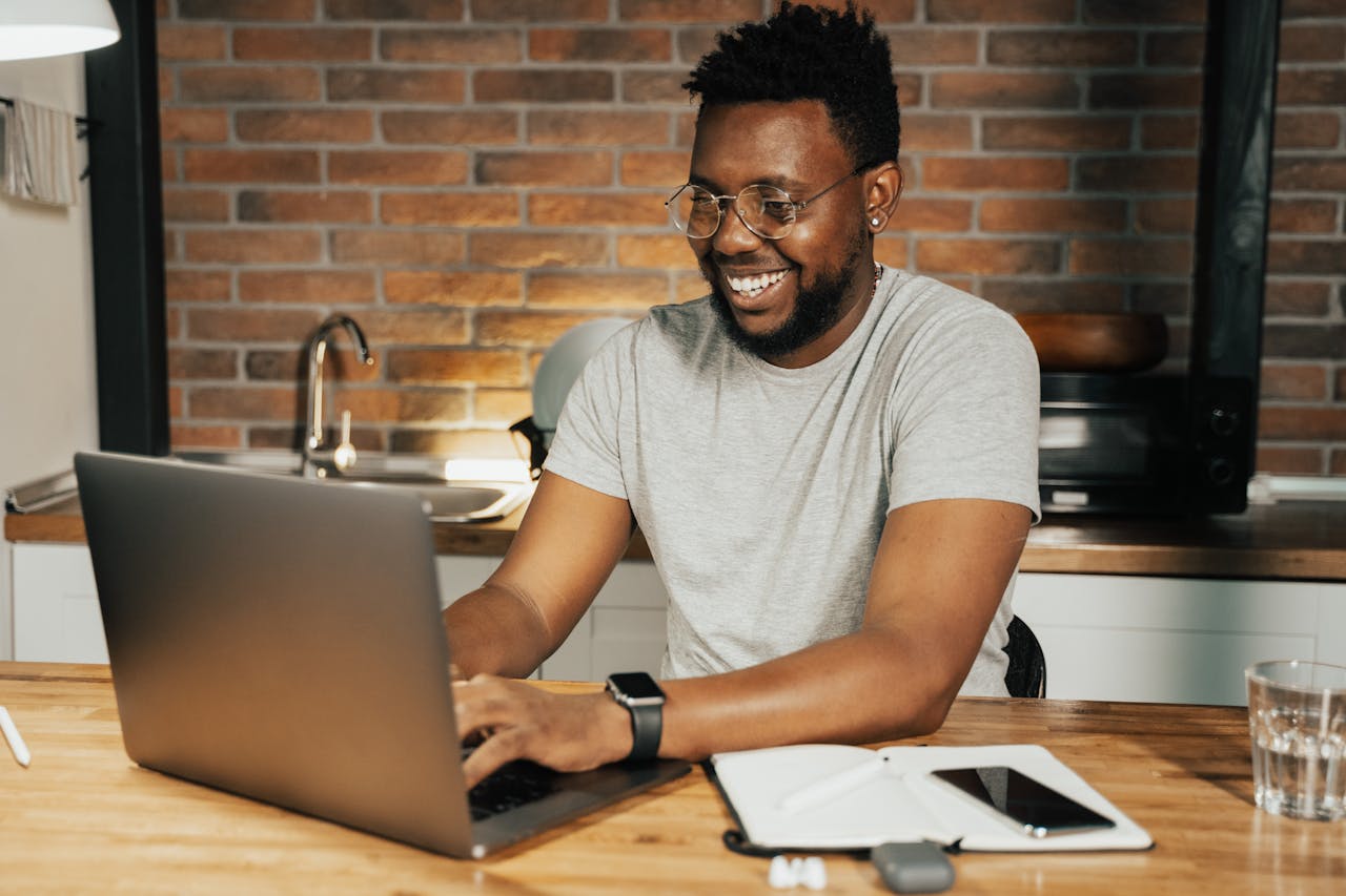 about-04 African American man smiling while working remotely on laptop from home office
