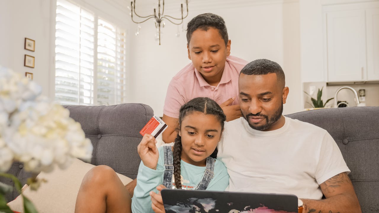 Father and children using a laptop for online shopping at home, bonding over e-commerce activities.