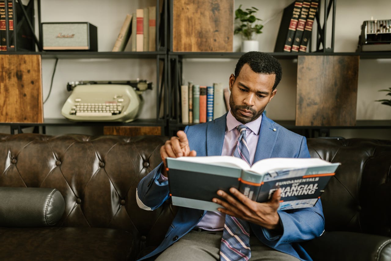 about-03 Focused businessman in a suit reading a financial planning book in office setting.
