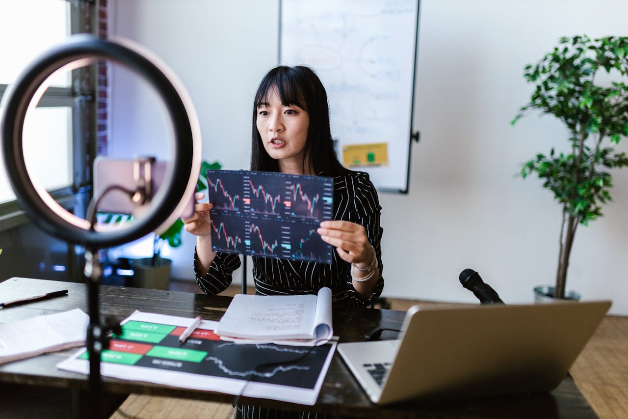 about-02 A woman vlogger discusses stock market trends using charts in a home studio.