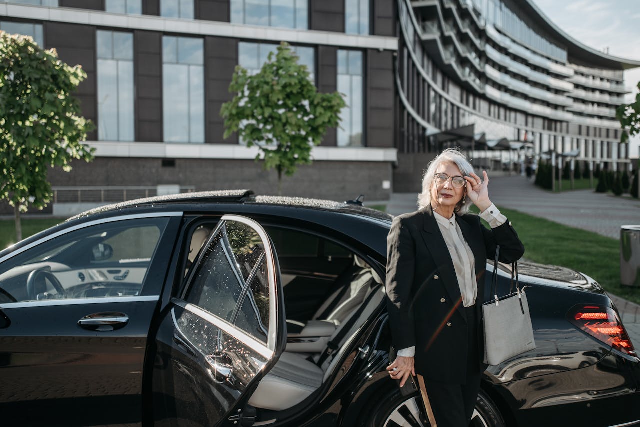Elegant senior woman in business attire stepping out of a luxury car in front of a modern office building.